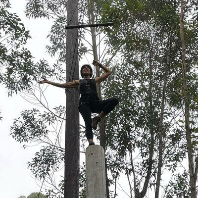 Maria standing in tree pose atop a ropes course pole